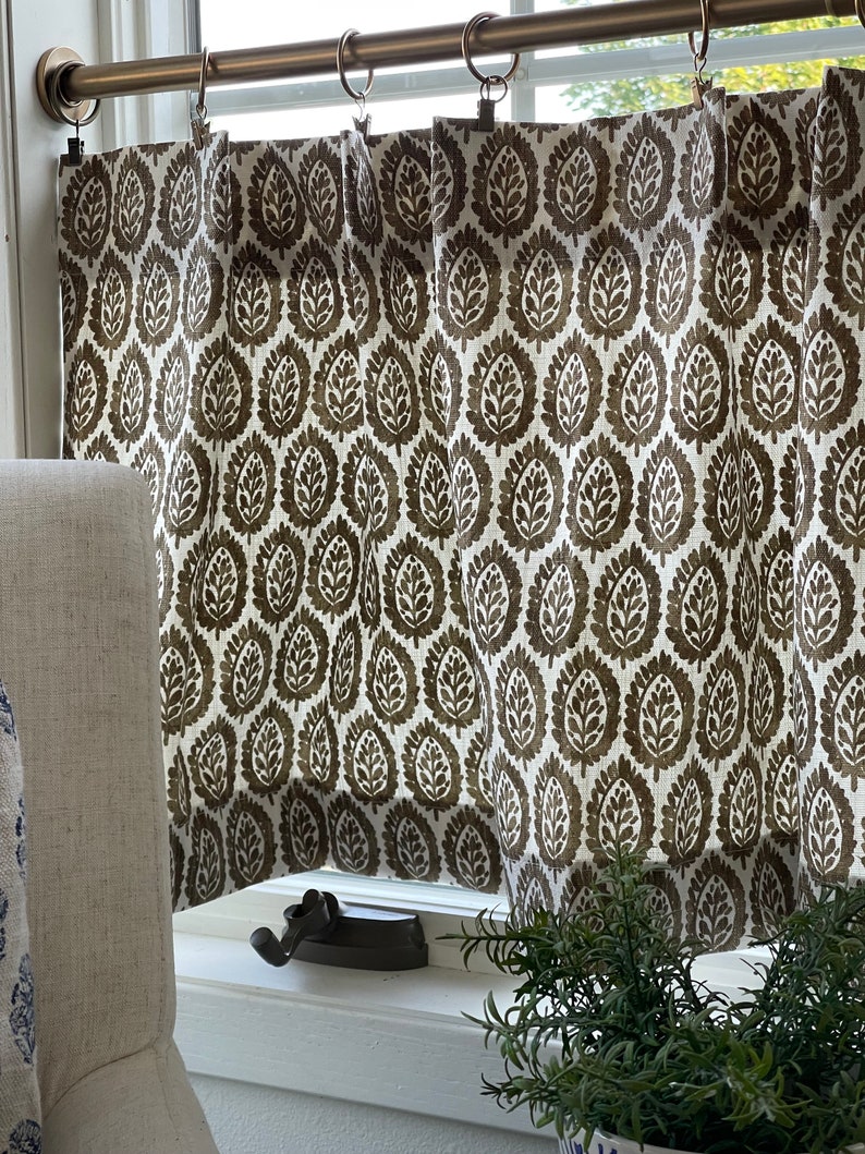 May include: A pair of brown and white patterned valance curtains with a brown leaf design. The curtains are hung on a brass curtain rod with rings.