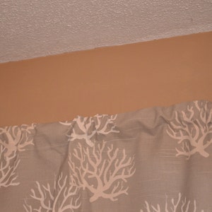 May include: A section of a curtain with a repeating white coral reef pattern on a light gray background. The curtain is hanging below a tan wall and a white ceiling.