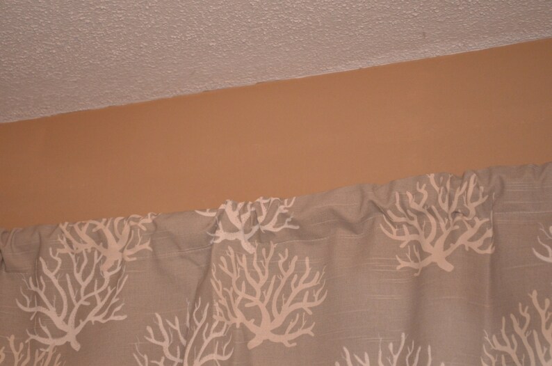 May include: A section of a curtain with a repeating white coral reef pattern on a light gray background. The curtain is hanging below a tan wall and a white ceiling.