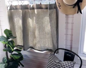 May include: A black and white vertical striped curtain hangs on a metal rod with rings. A straw hat with the text Hello Sunshine and a black ribbon sits nearby. A black and white gingham pillow rests on a black metal chair.