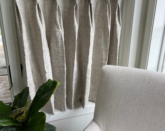 May include: A beige linen curtain with pleats hangs from a gold rod in front of a window. A white armchair sits in the foreground.
