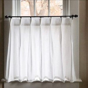May include: White sheer curtains with pleats hanging from a black curtain rod. The curtains are hung in a window with a white frame.