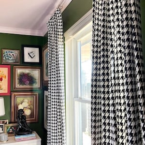 May include: Two black and white patterned curtains hang in a window with a green wall behind them. The curtains are made of a fabric with a houndstooth pattern.