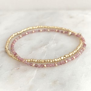 Pode incluir: Um bracelete delicado com duas fileiras de contas minúsculas. Uma fileira é feita de contas douradas, enquanto a outra fileira é feita de contas cor-de-rosa.