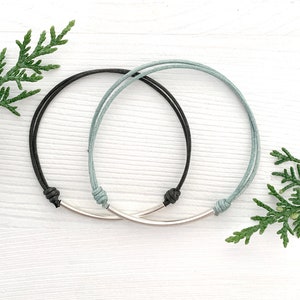 May include: Two friendship bracelets with a silver bar connector. One bracelet is black and the other is light blue.