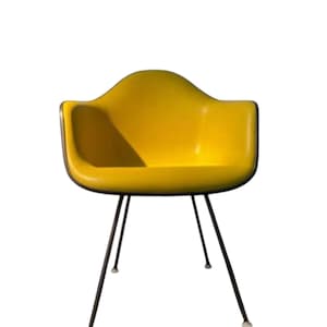May include: A bright yellow armchair with a curved back and armrests. The chair has a black trim and is supported by thin, black metal legs. The legs have small, white caps on the bottom. The chair is a modern design.