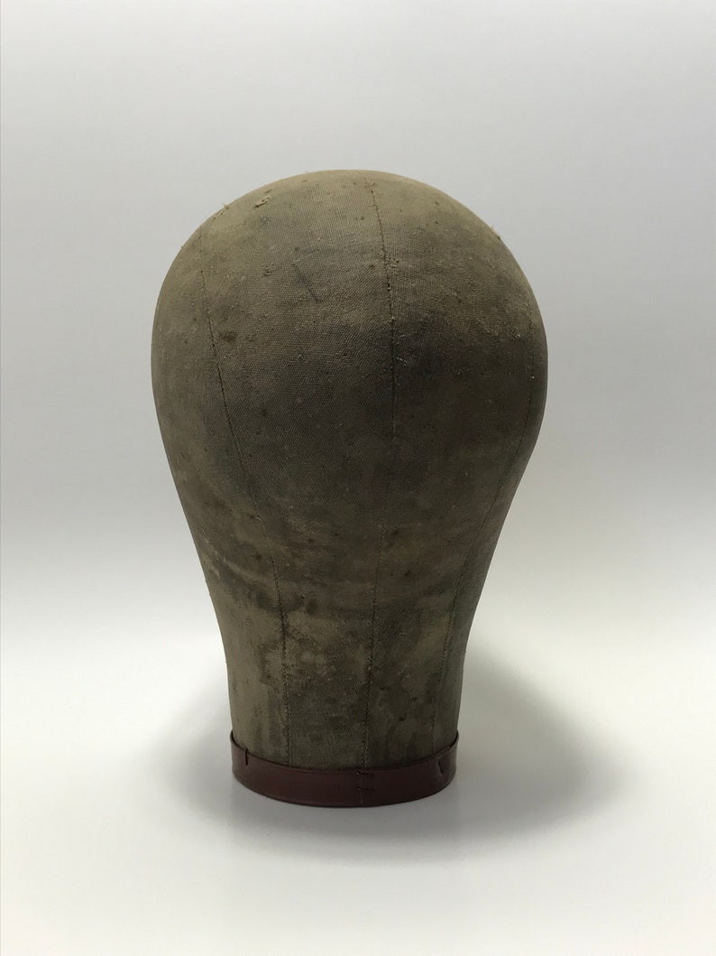 May include: A vintage fabric-covered dressmaker's head form with a brown base. The form is made of a sturdy material and has a slightly rounded shape.