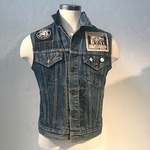 May include: A blue denim vest with patches and pins. The patches include "The Day The Music Died" and "Misery's Children".