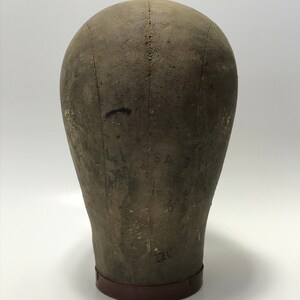 May include: A vintage, gray canvas dressmaker's head form with a brown leather base. The form has markings and numbers on the surface.