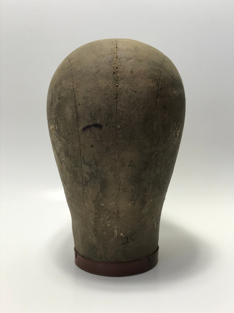 May include: A vintage, gray canvas dressmaker's head form with a brown leather base. The form has markings and numbers on the surface.