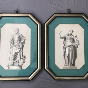 May include: Two ornate, octagonal, silver-framed pictures with a teal mat. The pictures feature black and white engravings of classical figures. The left picture shows a man holding a staff, and the right picture shows a woman holding a child.