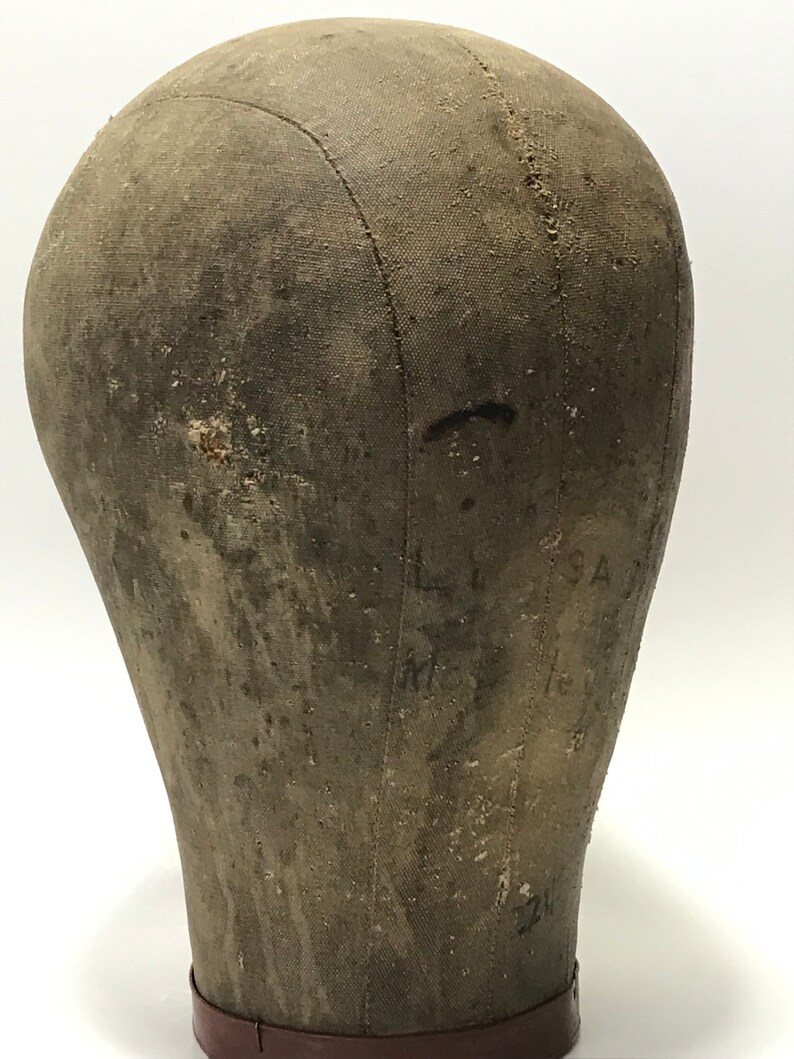 May include: A vintage, brown canvas dressmakers head form with a brown leather base. The form has visible stitching and markings.