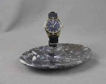 May include: A black and gold wristwatch with a black leather band on a black and white marble watch stand.