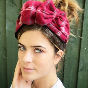 May include: A red and white plaid headband with a large bow. The headband is made of soft, fuzzy fabric.