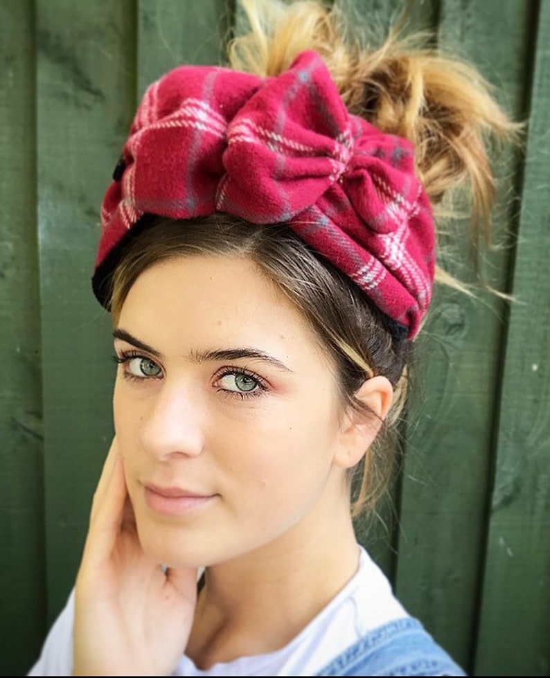 May include: A red and white plaid headband with a large bow. The headband is made of soft, fuzzy fabric.
