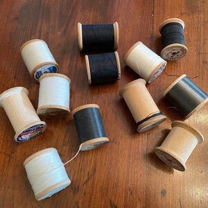 May include: A collection of wooden spools of thread in white, black, and gray. The spools are arranged on a wooden surface.