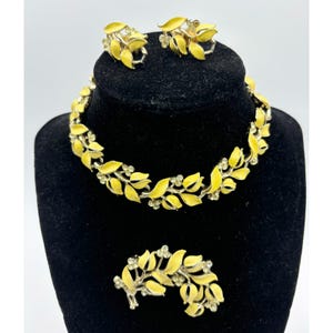 May include: A vintage jewelry set featuring a necklace, earrings, and a brooch. The set has a gold-tone metal base with bright yellow enamel leaf designs and small clear rhinestone accents. The jewelry is displayed on a black velvet bust.