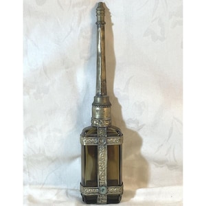 May include: An antique perfume bottle with a long, slender metal applicator. The bottle is rectangular, made of amber-colored glass, and adorned with ornate metal filigree. The metal applicator extends upwards, adding to the bottle's elegant design.