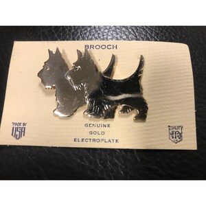 以下が含まれることがあります： 2匹のスコティッシュテリアがデザインされた金メッキのブローチ。ブローチは、「BROOCH」、「GENUINE GOLD ELECTROPLATE」、「MADE IN USA」、「QUALITY」と書かれたカードの上に置かれています。
