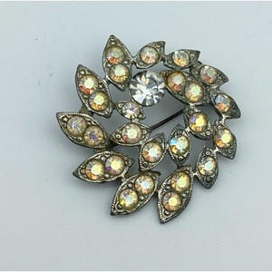 May include: A silver tone brooch with a large clear rhinestone in the center surrounded by smaller iridescent rhinestones set in a leaf design.