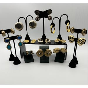 Könnte beinhalten: Eine Sammlung von Vintage-Ohrringen, die auf schwarzen Ständern ausgestellt sind. Die Ohrringe variieren im Stil, darunter goldene Creolen, strukturierte Ohrstecker und Ohrhänger mit blauen und türkisfarbenen Steinen. Einige Ohrringe haben aufwendige Designs.