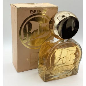 May include: Vintage Faberge Babe spray cologne bottle with its original box. The bottle is clear with a gold-coloured label and a gold-coloured cap. The box is tan with gold lettering and a gold-coloured logo.