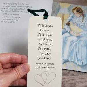 Pu&ograve; includere: Un segnalibro rettangolare color bianco sporco con un nastro verde scuro in alto. Il testo recita: "I'll love you forever. I'll like you for always. As long as I'm living, my baby you'll be." Include anche "Love You Forever by Robert Munsch", due contorni di cuori, "Baby Austin's Shower" e "November 7, 2020".
