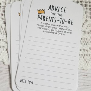 May include: A stack of white cards with black lines and the text "ADVICE for the PARENTS-TO-BE" with a gold crown above the text. The text continues with "A wild one is on the way! Please share your best advice, well wishes, and words of love for Haylee & Dyllon." The bottom of the card says "WITH LOVE,".