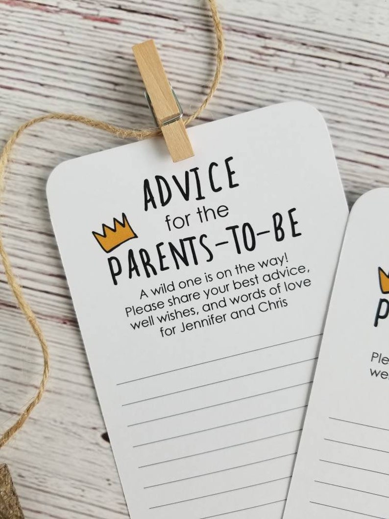 May include: A white card with black text that reads "Advice for the Parents-to-Be". A yellow crown is above the text. The card has lined spaces for writing advice for the new parents. A wild one is on the way! Please share your best advice, well wishes, and words of love for Jennifer and Chris.