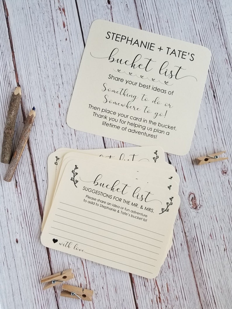 Op de afbeelding: Een stapel cr&egrave;mekleurige kaarten met zwarte tekst die "bucket list" en "Suggesties voor de heer en mevrouw" luidt. De kaarten zijn ontworpen voor een bruiloft of verlovingsparty en zijn bedoeld om door gasten te worden gebruikt om idee&euml;n voor de bucketlist van het paar op te schrijven.