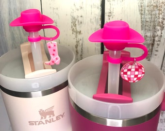 May include: Two stainless steel travel mugs with pink lids and pink silicone straw covers. The lids have a pink cowboy hat design. One mug is white with the Stanley logo and the other is pink with the Stanley logo.