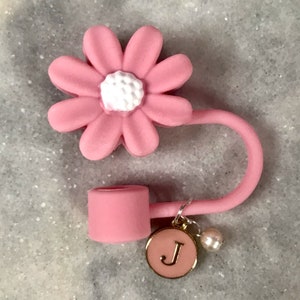 May include: Pink silicone phone charm with a daisy flower design and a small charm with the letter "J" hanging from it.