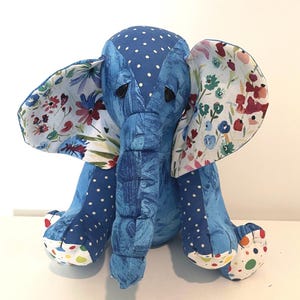 May include: A blue stuffed elephant with white polka dots on its head and legs. The elephant's ears are patterned with a floral design in shades of red, blue, and white. The elephant is sitting upright.
