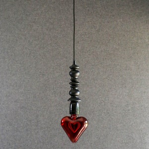 May include: A red heart-shaped light bulb hangs from a black cord and a black beaded fixture.