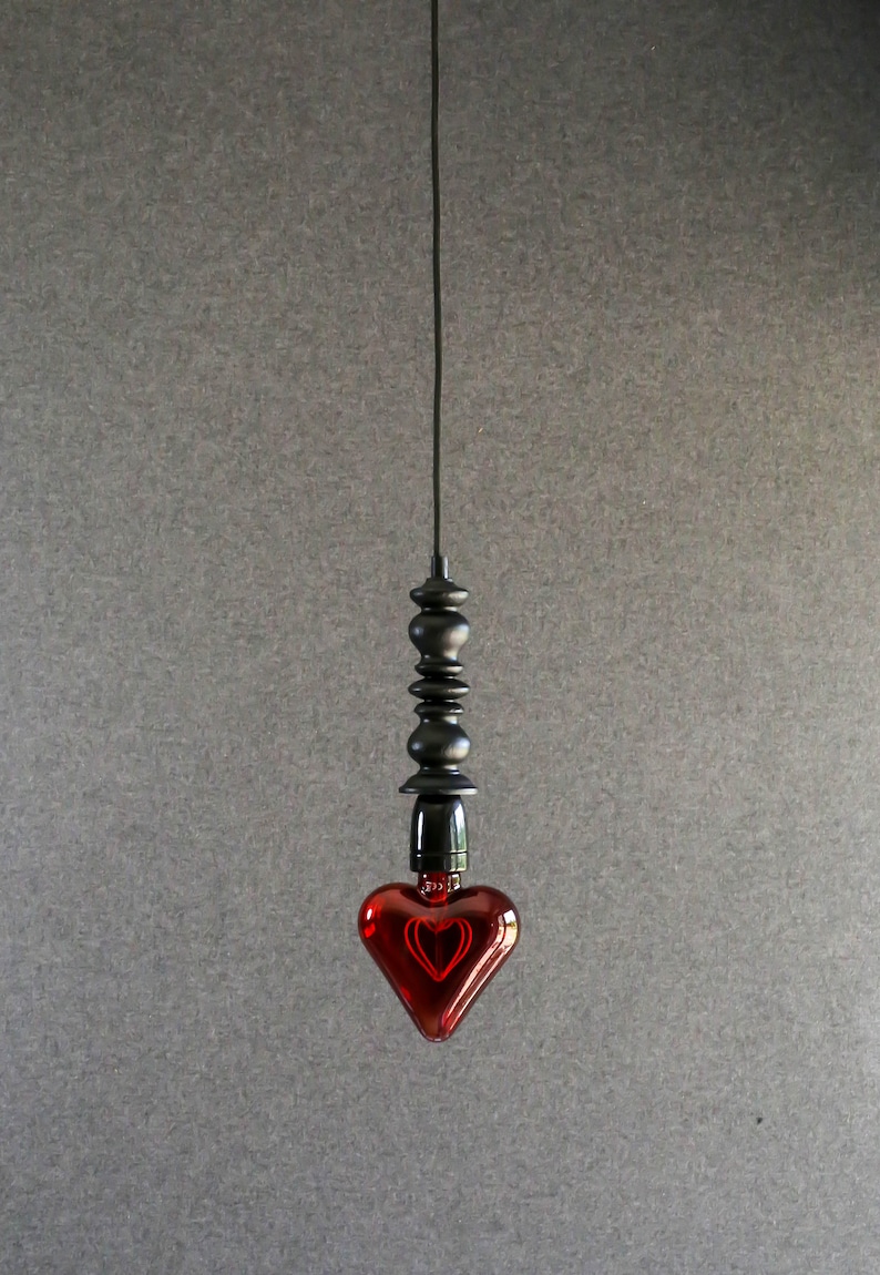 May include: A red heart-shaped light bulb hangs from a black cord and a black beaded fixture.