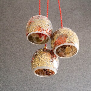 May include: Three gold and red mosaic glass pendant lights hanging from red cords against a gray background.