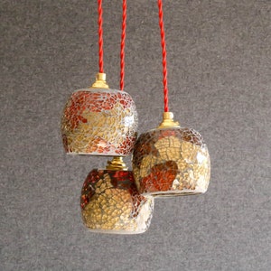 May include: Three hanging pendant lights with red cords. The glass shades are round and made of mosaic tiles in shades of gold, brown, and red.
