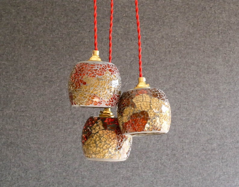 May include: Three hanging pendant lights with red cords. The glass shades are round and made of mosaic tiles in shades of gold, brown, and red.