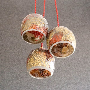 May include: Three hanging light fixtures with red cords. The light fixtures are made of glass and have a mosaic pattern of gold and red tiles.
