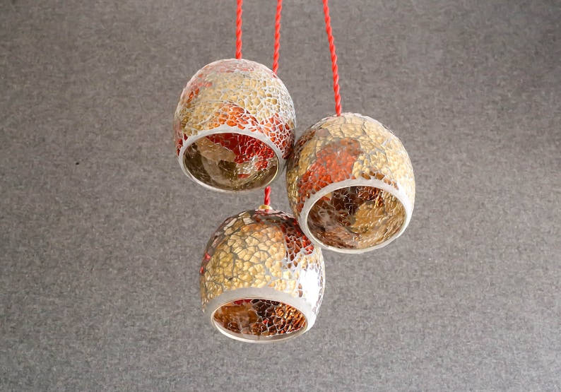 May include: Three hanging light fixtures with red cords. The light fixtures are made of glass and have a mosaic pattern of gold and red tiles.