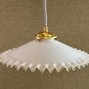 以下が含まれることがあります： フリルエッジの白いガラスペンダントライト。照明器具は真鍮色の金属製金具と灰色の布で覆われたコードが付いています。シェードはソフトホワイトで、スカラップエッジが付いています。