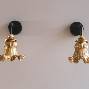 Puede incluir: Dos apliques de pared dorados con accesorios de metal negro y pantallas de lámpara con volantes.