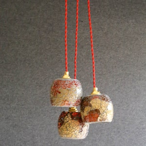 May include: Three glass pendant lights with red and gold mosaic patterns hang from red cords against a gray background.