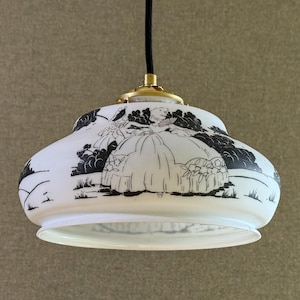Puede incluir: Lámpara colgante blanca con una ilustración en blanco y negro de un paisaje. La lámpara tiene forma redondeada, una parte superior de color latón y un cable negro.