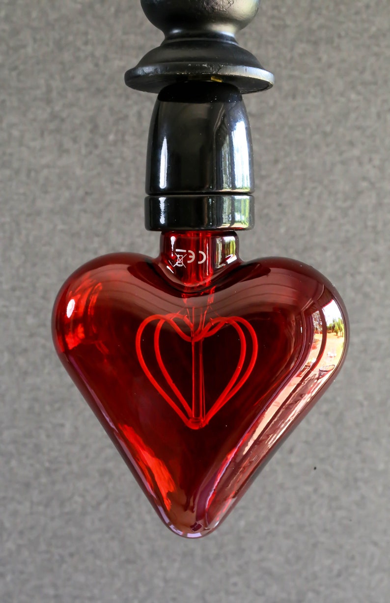 May include: A red heart-shaped light bulb with a black socket and a visible filament in the shape of a heart.