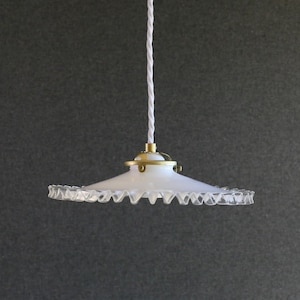 以下が含まれることがあります： フリルエッジと真鍮のアクセントが付いた白いガラスペンダントライト。白いねじれたコードからライトが吊り下げられています。装飾的なシーリングライト器具。