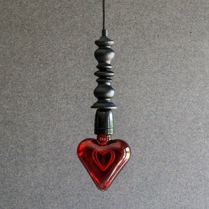 May include: A black pendant light with a red heart-shaped glass bulb. The light fixture has a series of black finials.