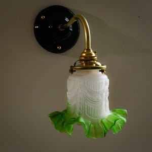 Puede incluir: Una lámpara de pared vintage con una base de metal negro y una pantalla de vidrio verde y blanco. La pantalla tiene un borde rizado y un diseño decorativo.