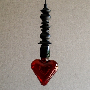 May include: A red heart-shaped glass light bulb hangs from a black metal cord with a decorative finial.