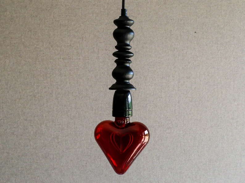 May include: A red heart-shaped glass light bulb hangs from a black metal cord with a decorative finial.